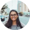 A woman with glasses and a grey shirt smiles warmly, conveying a sense of happiness and friendliness.